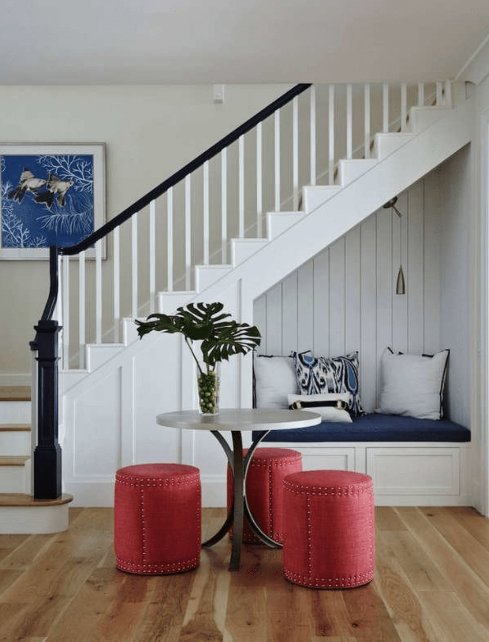 entryway view of staircase with cushioned bench inside nook behind round table with cylindrical red stools