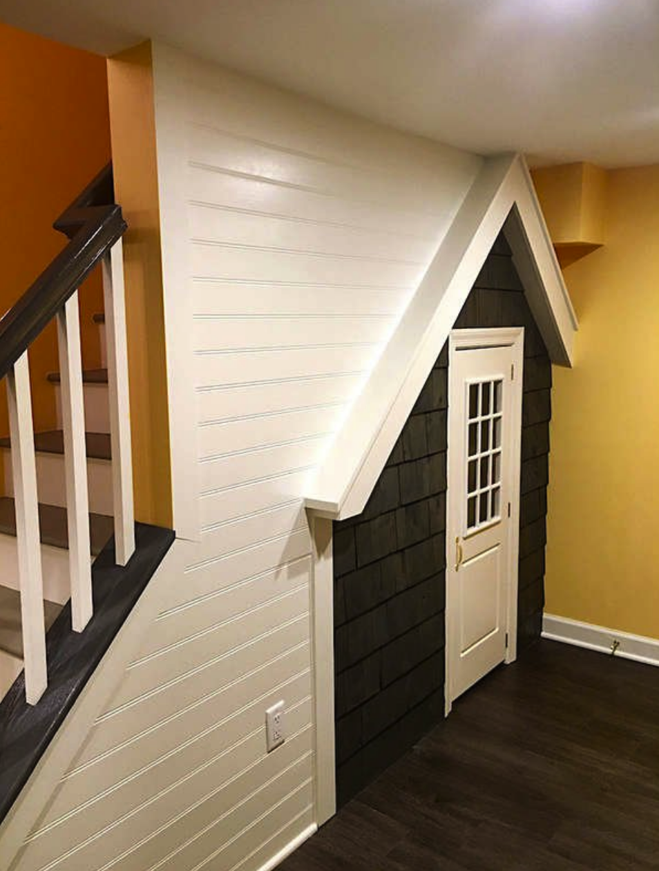 angular view of children's small house facade underneath a staircase in a basement with yellow walls