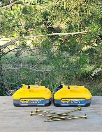 DeWalt PowerStack Batteries sitting outdoors on a workbench next to long screws