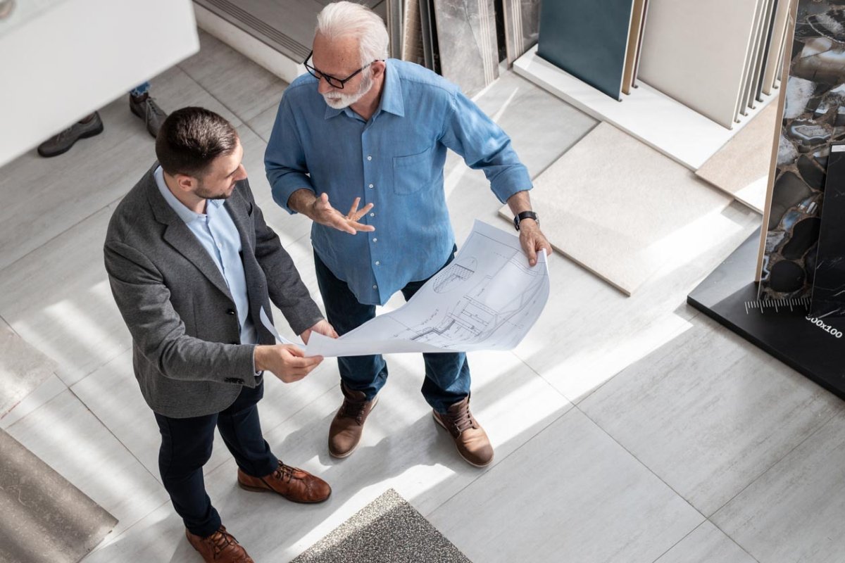 An aerial view of two people holding a blueprint and having an animated discussion.