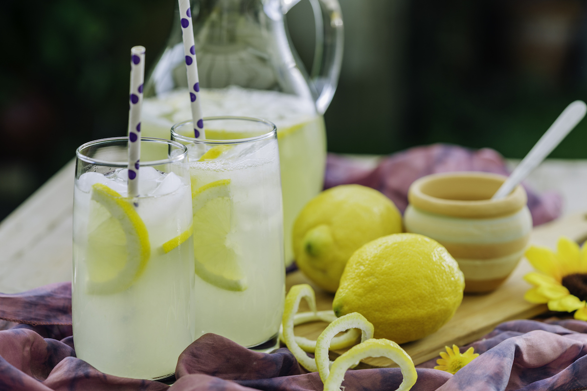 A pitcher of fresh homemade lemonade alongside lemons and full glasses of lemonade.