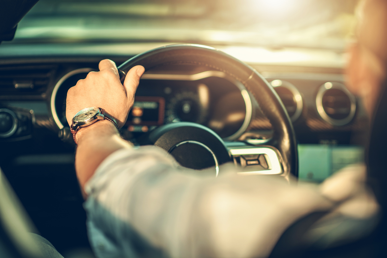 hands on dark colored steering wheel lit by hot sun