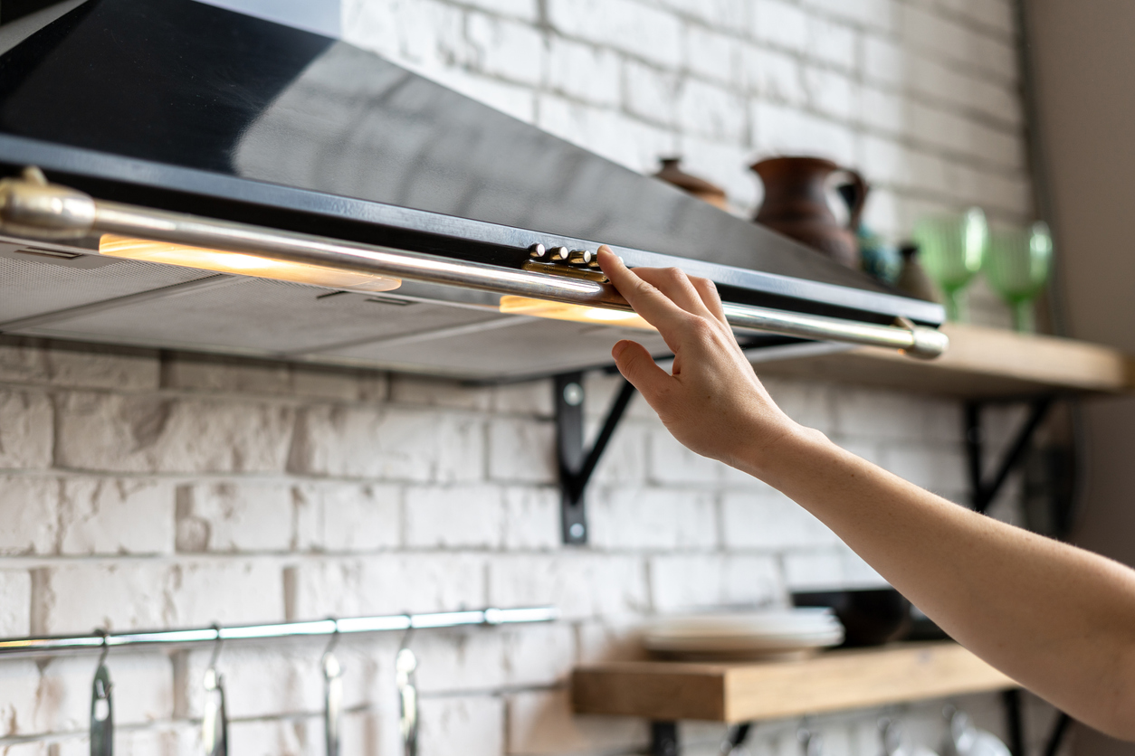 woman's hand pressing button on black range hood in kitchen to turn it on