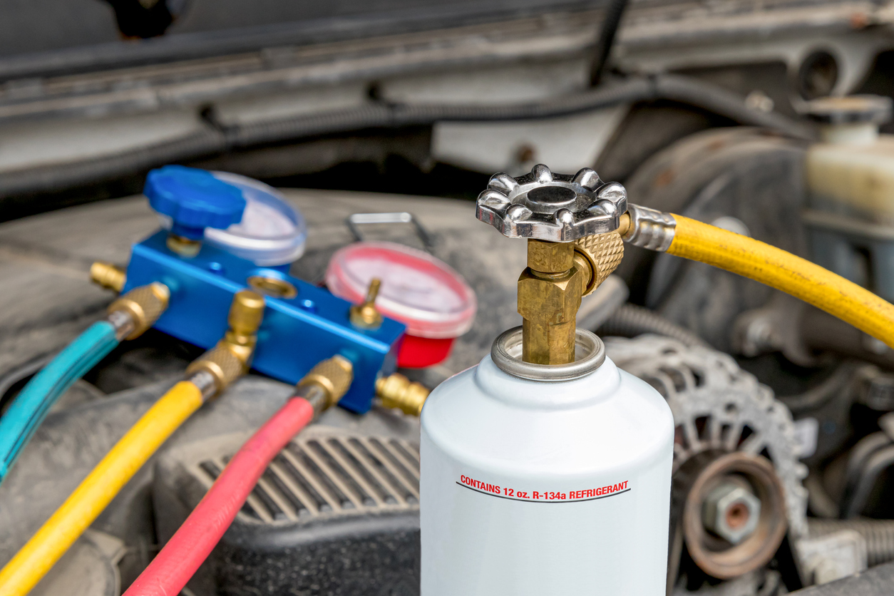 close shot on canister of refrigerant and car engine with open hood