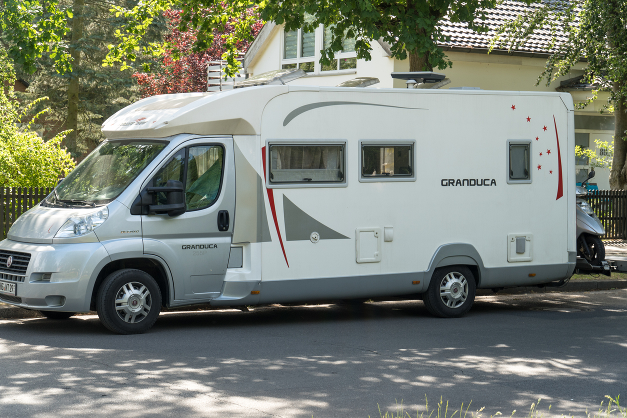 large white camper vehicle parked on shady street in residential neighborhood