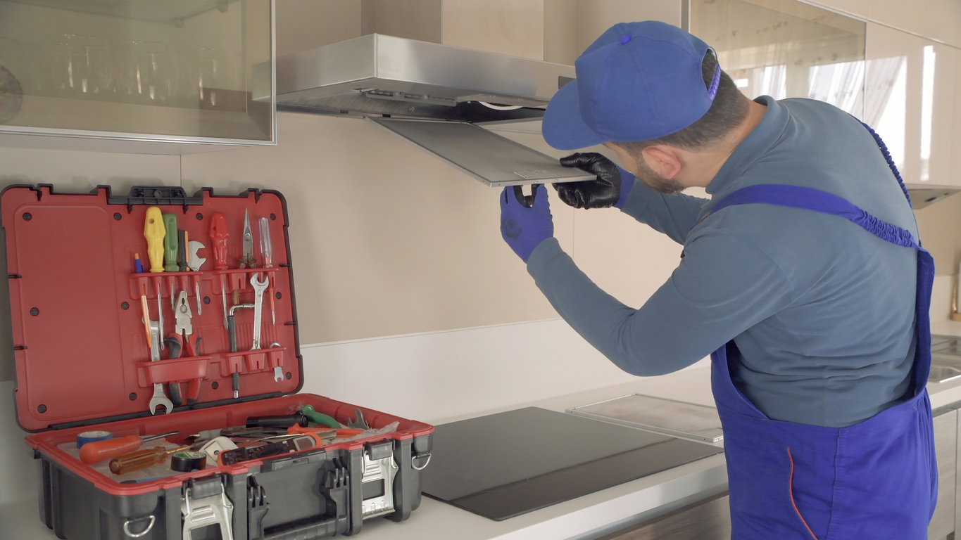 service man in blue uniform opening range hood in kitchen to check fan