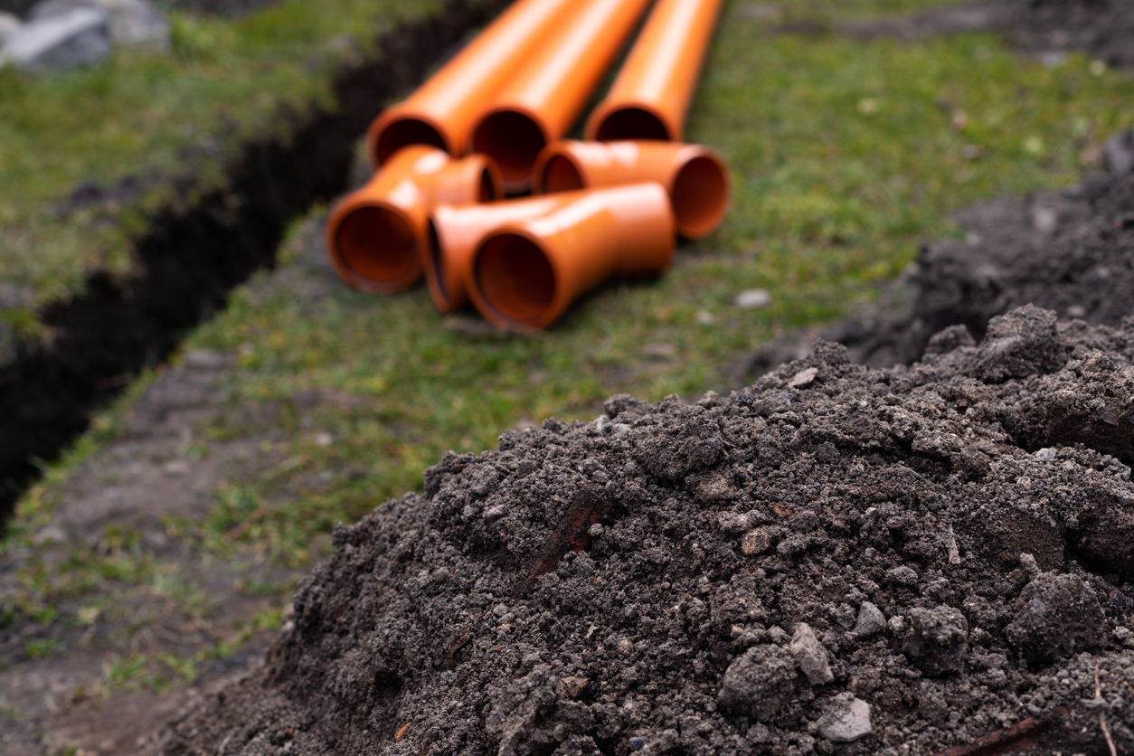 orange piping stacked next to ditch in lawn