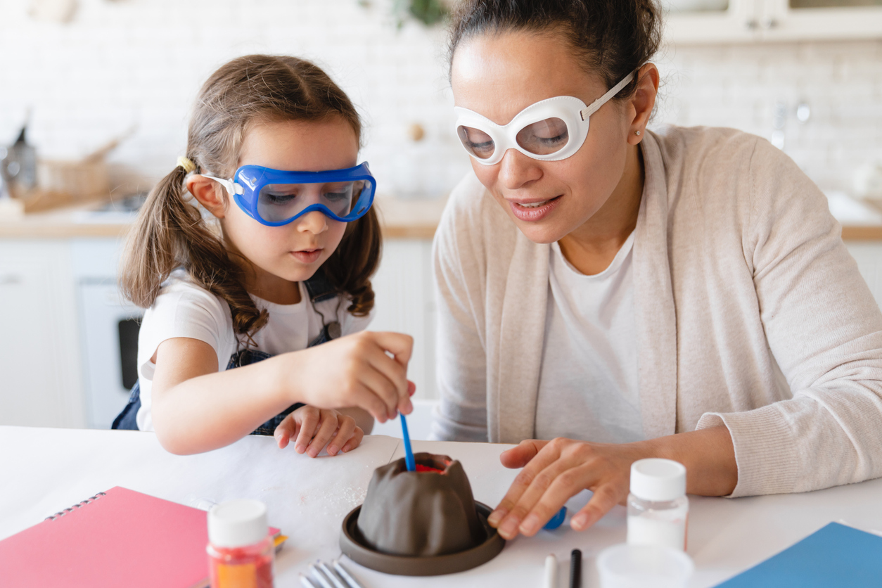 Young mother helping her daughter with science experiment with volcano eruption at home kitchen. Chemistry lab at home. Baking soda for project