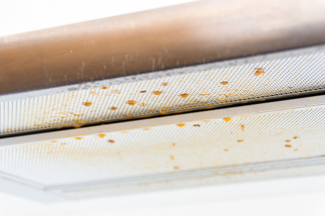 close up on white screen of range hood with orange grease splatters on it