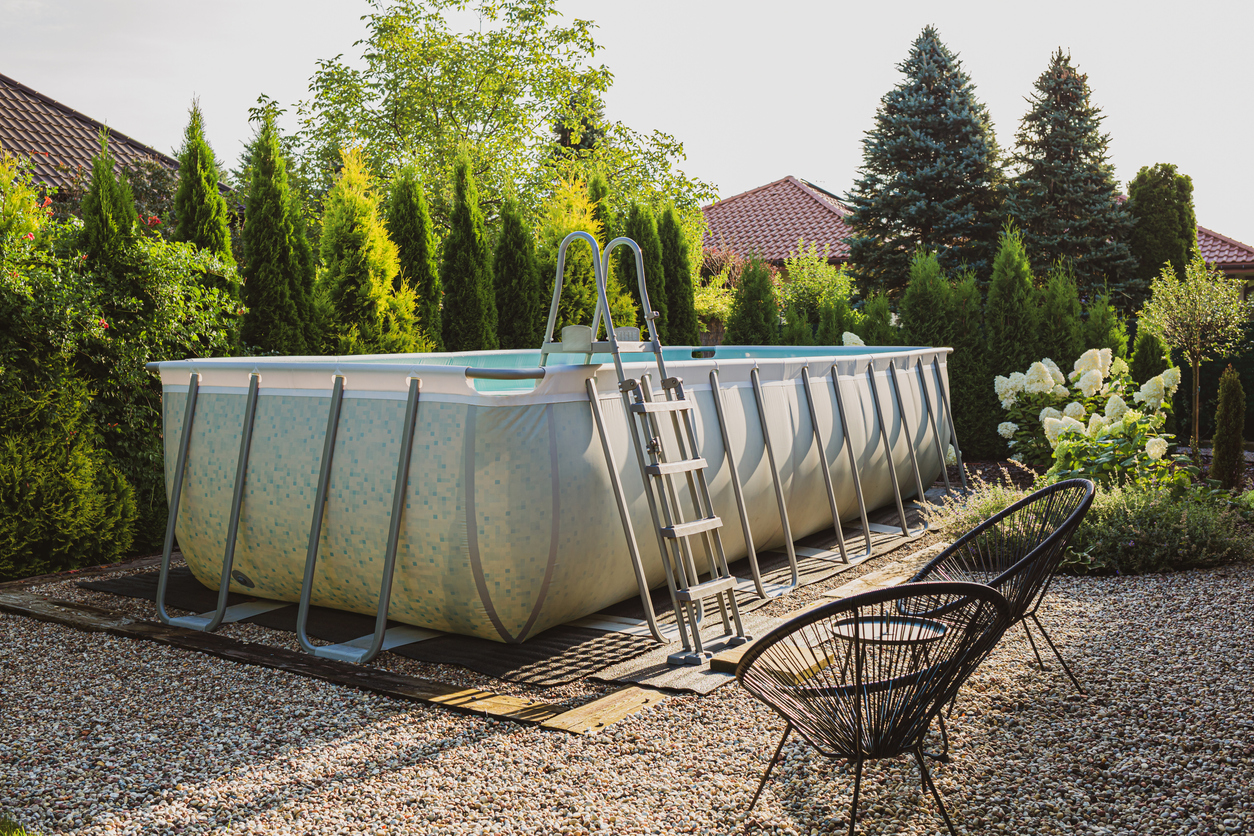 Long, above ground, rectangular, rack (frame) swimming pool outdoor in the pebble (gravel) garden nook. Summer holiday (vacation) and recreation.