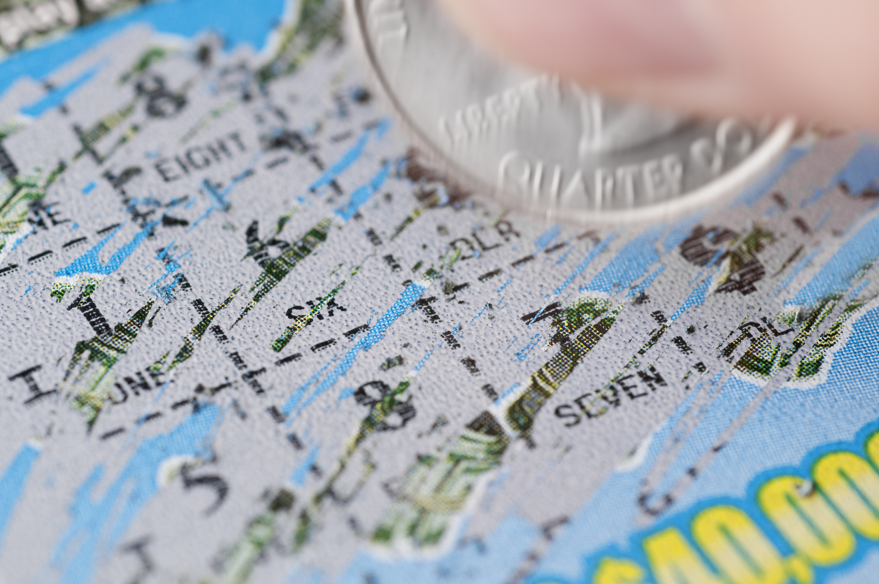 close up of lottery ticket being scratched with silver coin held between two fingers