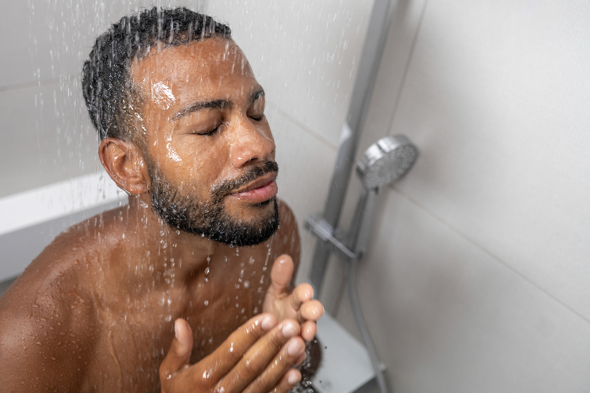 Man with eyes closed taking shower with his face in the water.