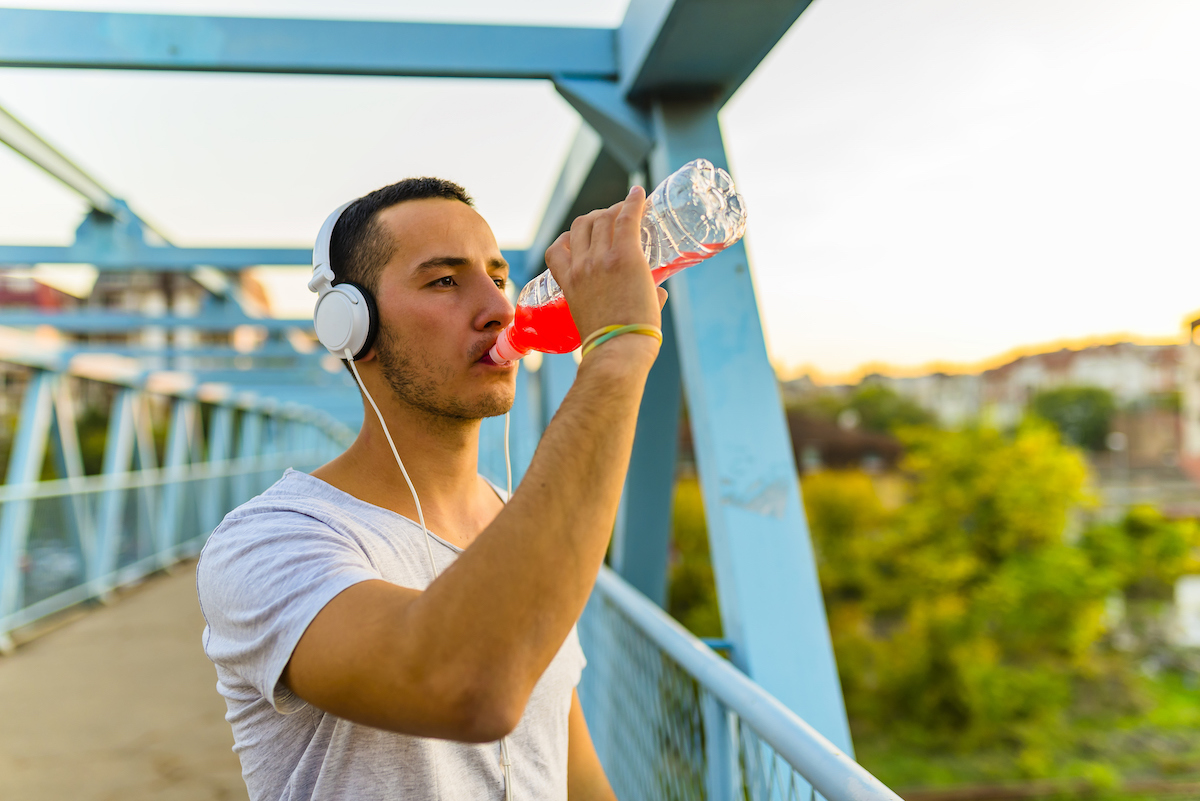Young man standing on a bridge drinking a sports drink.