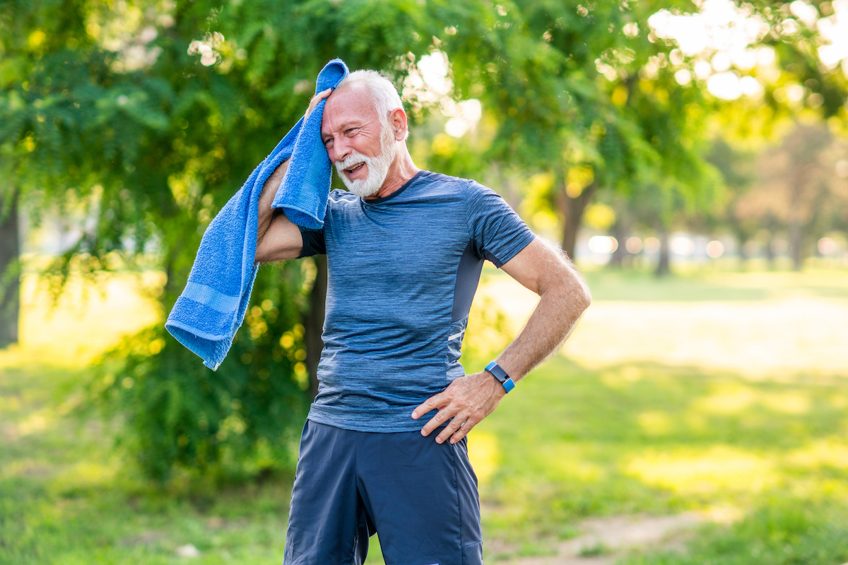 Senior man wiping his forehead with a towel after exercising in the park.