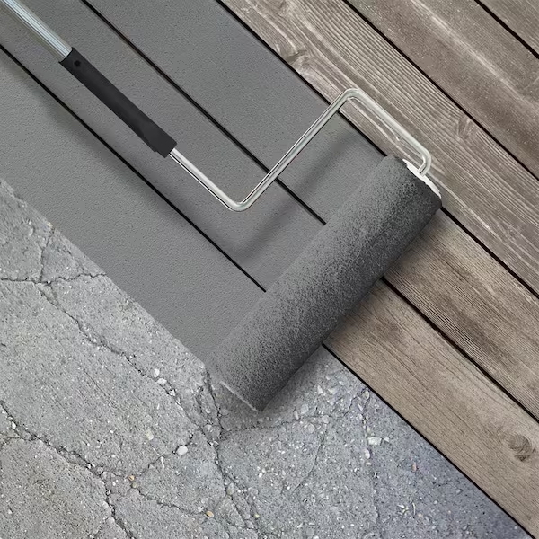 A paint roller with grey paint on it rolls between wood decking and concrete flooring.