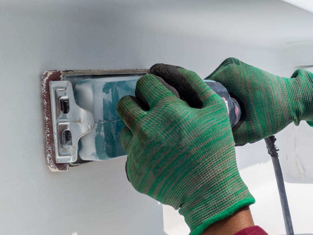 Using a Ponceuse Vibrante or Orbital Sander to scrub surface intermediate fire proof paint before painting top coat.