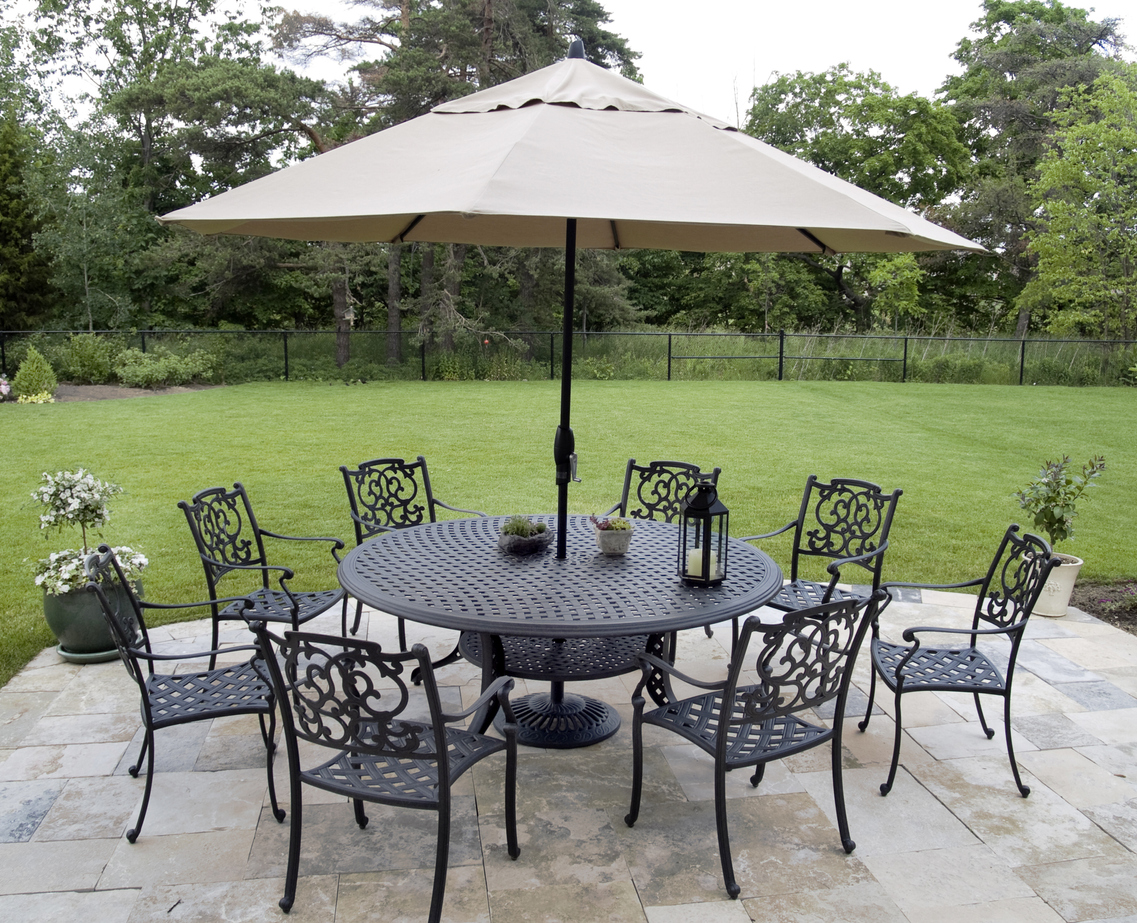 A patio umbrella set up through the center of a metal patio set before a large grassy yard