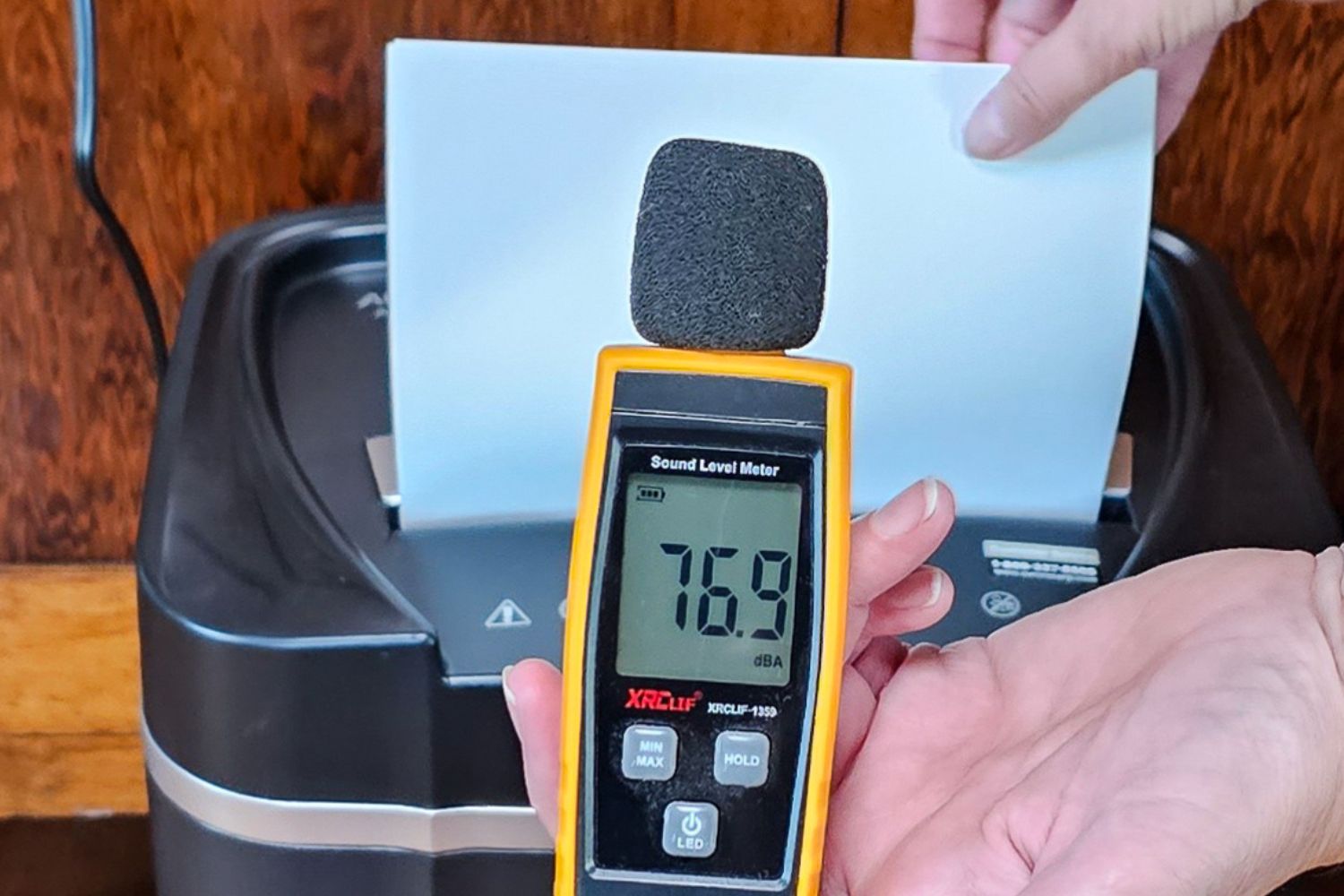 A decibel tester next to the Aurora paper shredder showing that it operates at 76.9 decibels