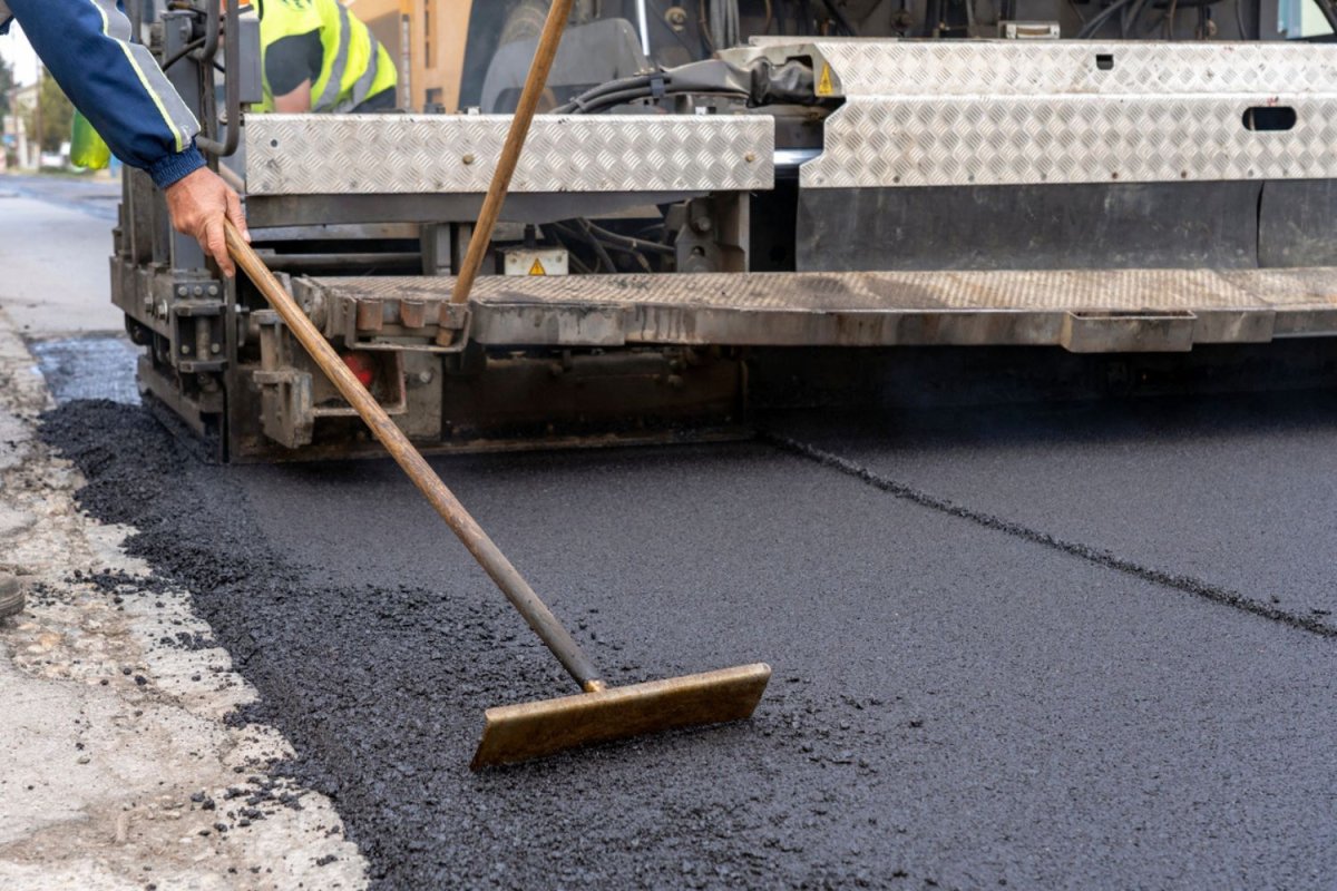 A construction crew paves a driveway using heavy machinery.