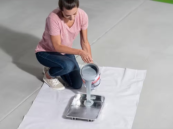 Woman pours concrete floor paint from a gallon can into a paint tray.