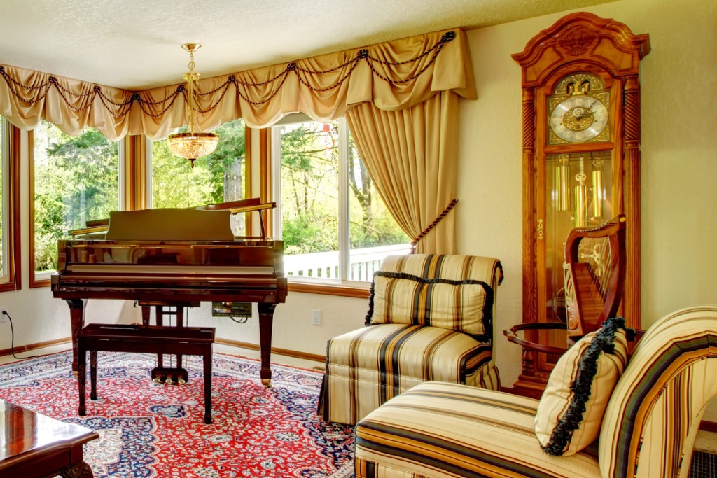 Bright living room with old fashioned couch and chairs, wooden coffee table, grand piano and antique oak grandfather clock