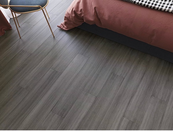 Grey engineered bamboo flooring with the corner of a red bed comforter and chair in frame.