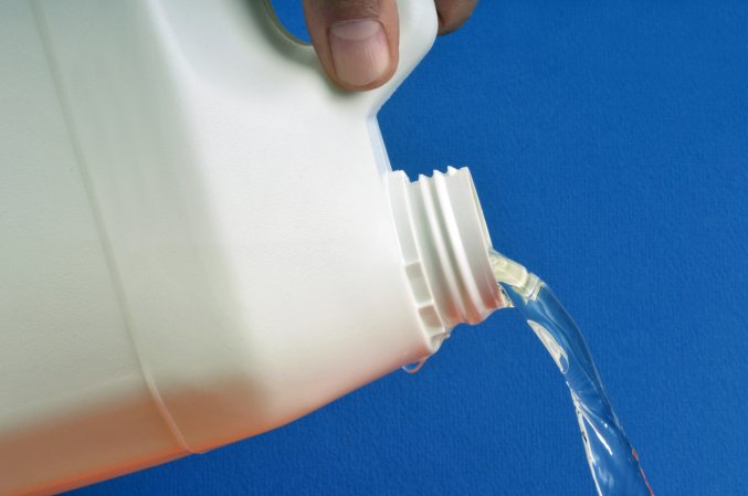 a large white bottle pouring a stream of clear bleach with a blue background