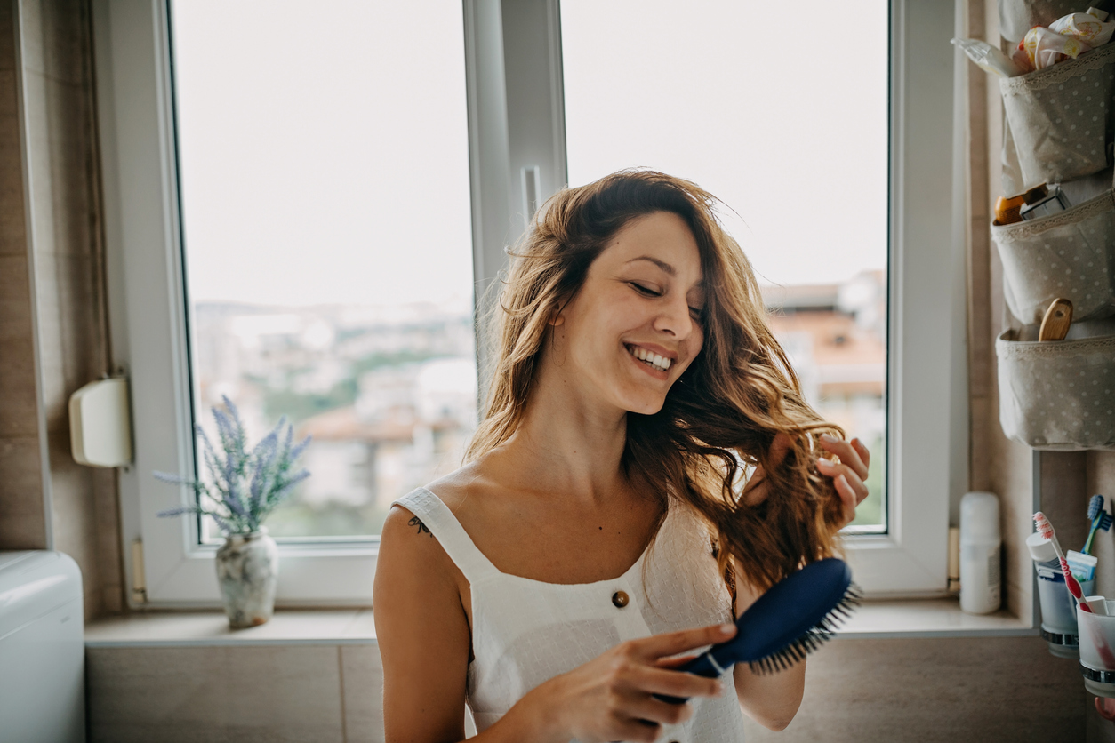 young woman in bathroom brushing her hair