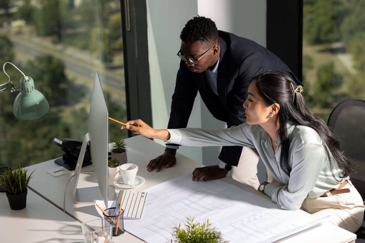 two architects in office working at desk with computer and blueprints