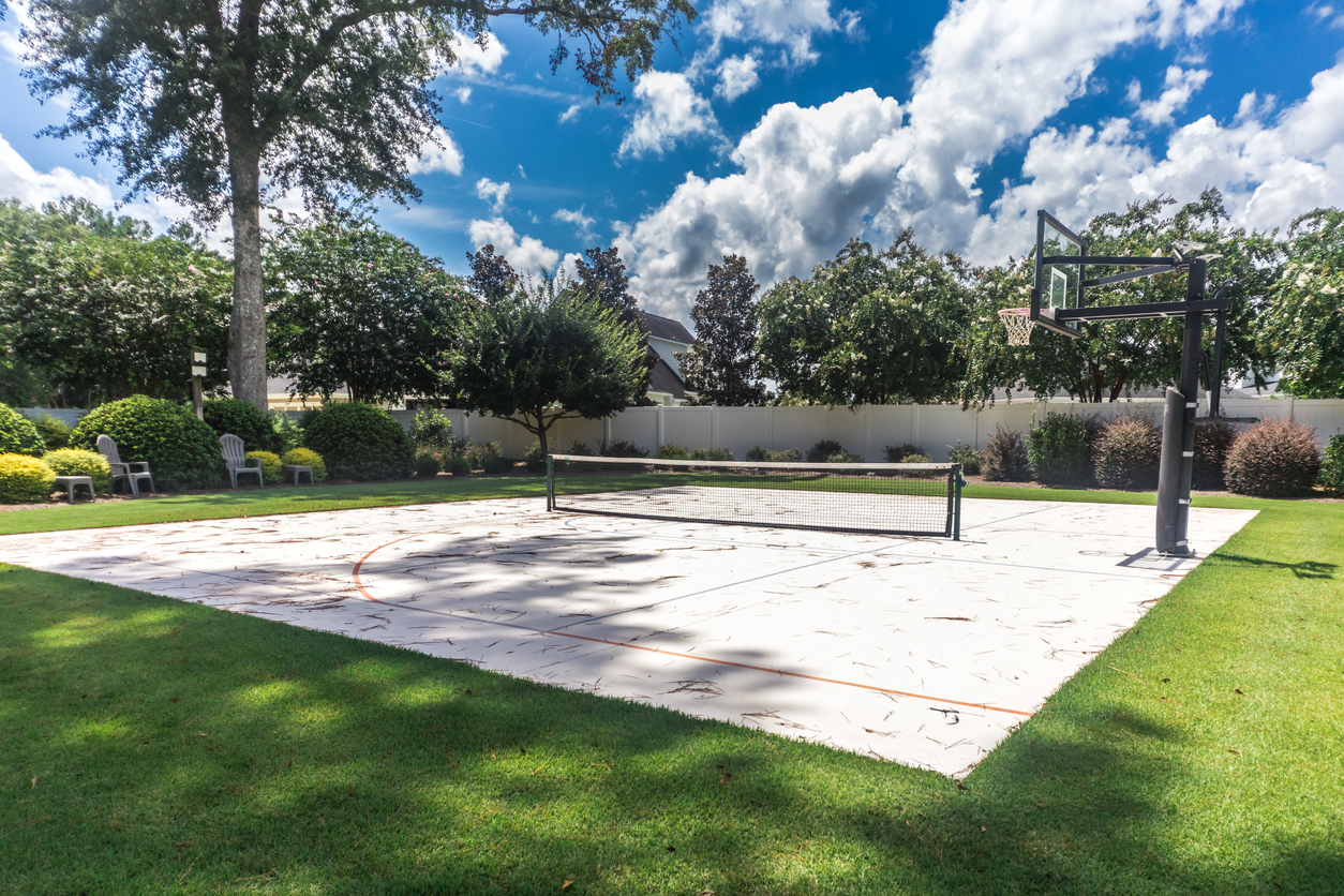 A large backyard with green grass and a basketball court that has been made into a home pickleball court.