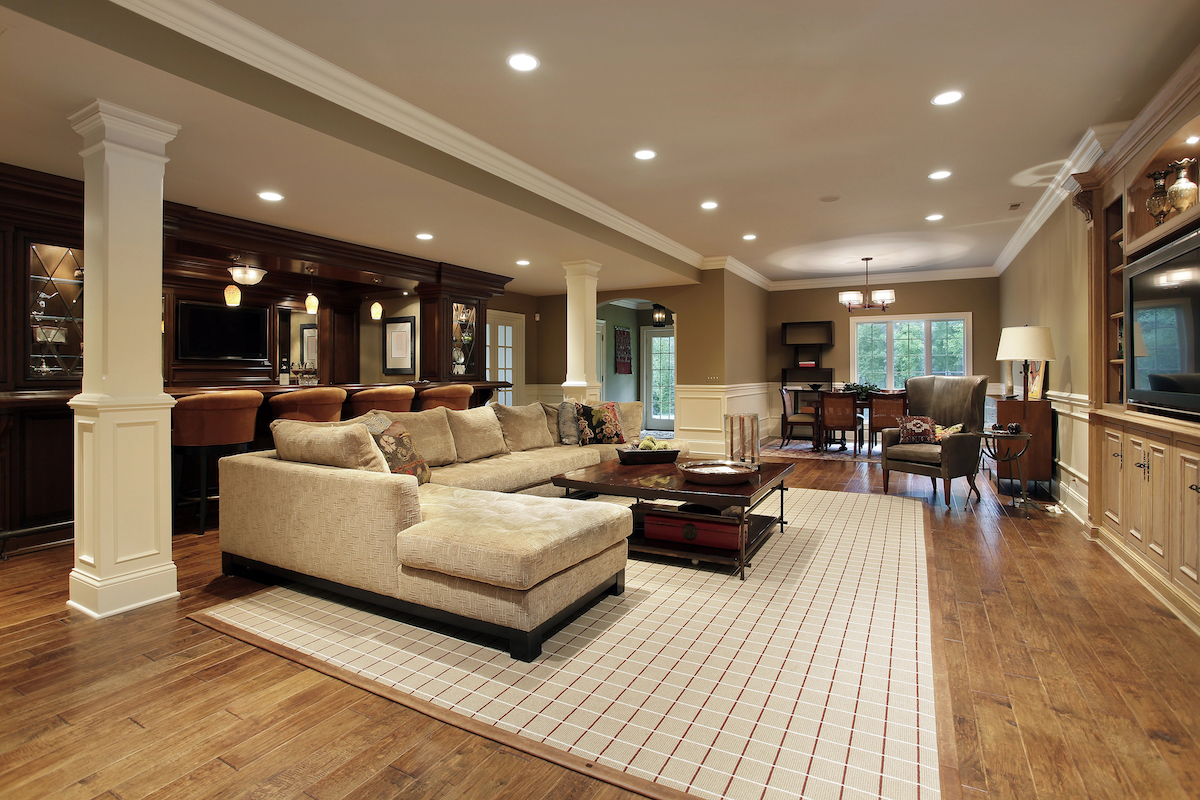 Luxurious finished basement with large sectional couch, area rug, and polished wood-look floors.