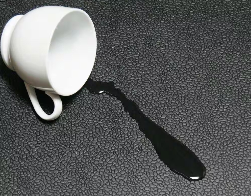 A white teacup lay on its side, with some liquid spilled out, atop black rubber flooring.