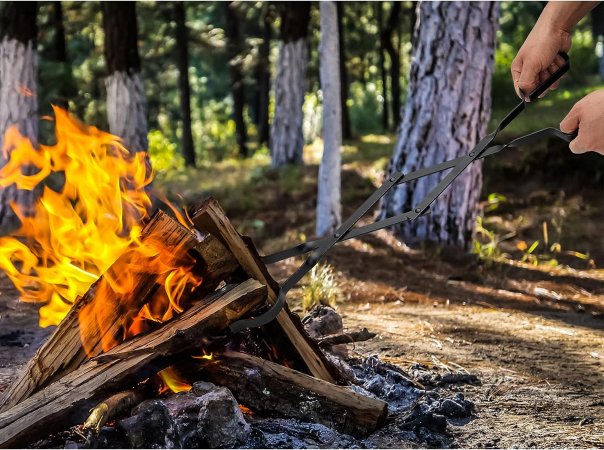 A person using the best fire pit tongs to reposition a log in a campfire.