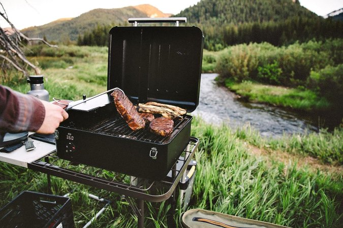 A person using the Traeger Ranger Electric Portable Pellet Grill to cook near a stream.