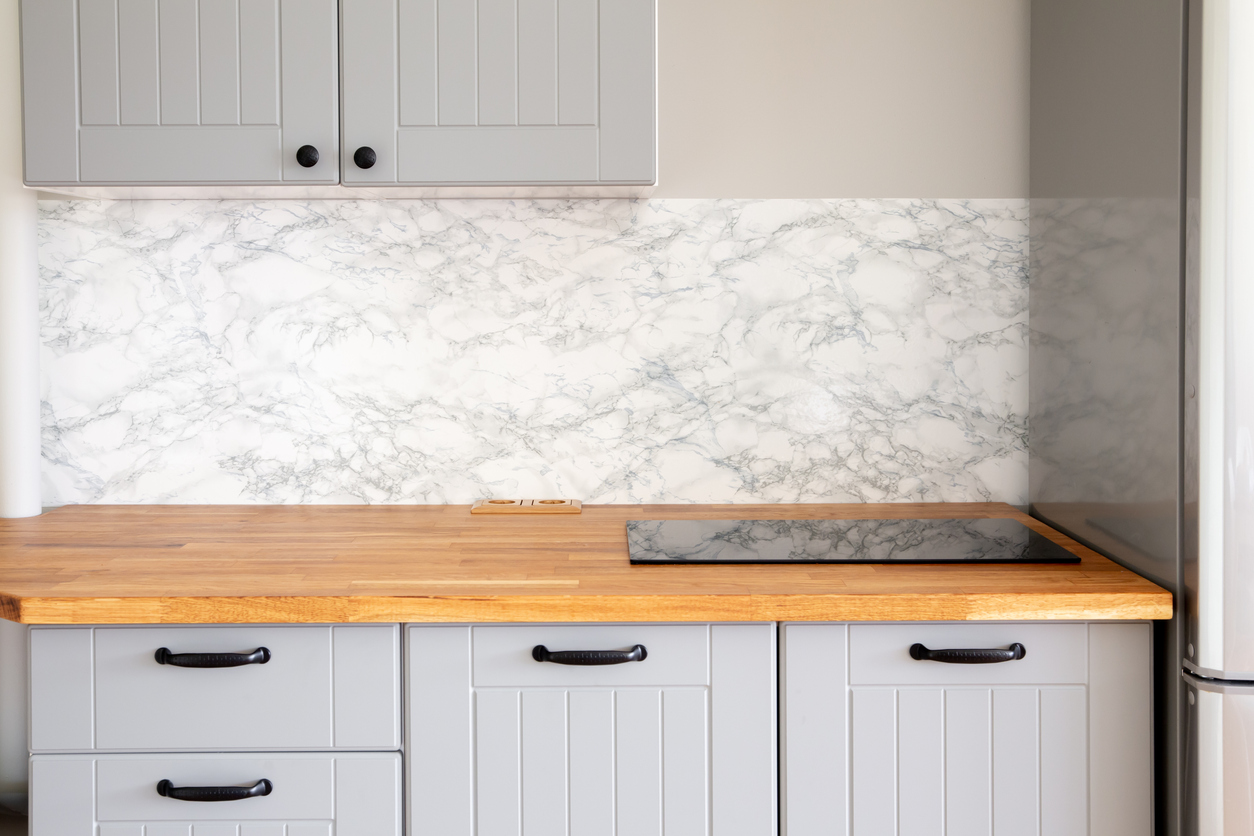 A kitchen with butcher block countertops, gray cabinets, black pulls, and an induction stovetop