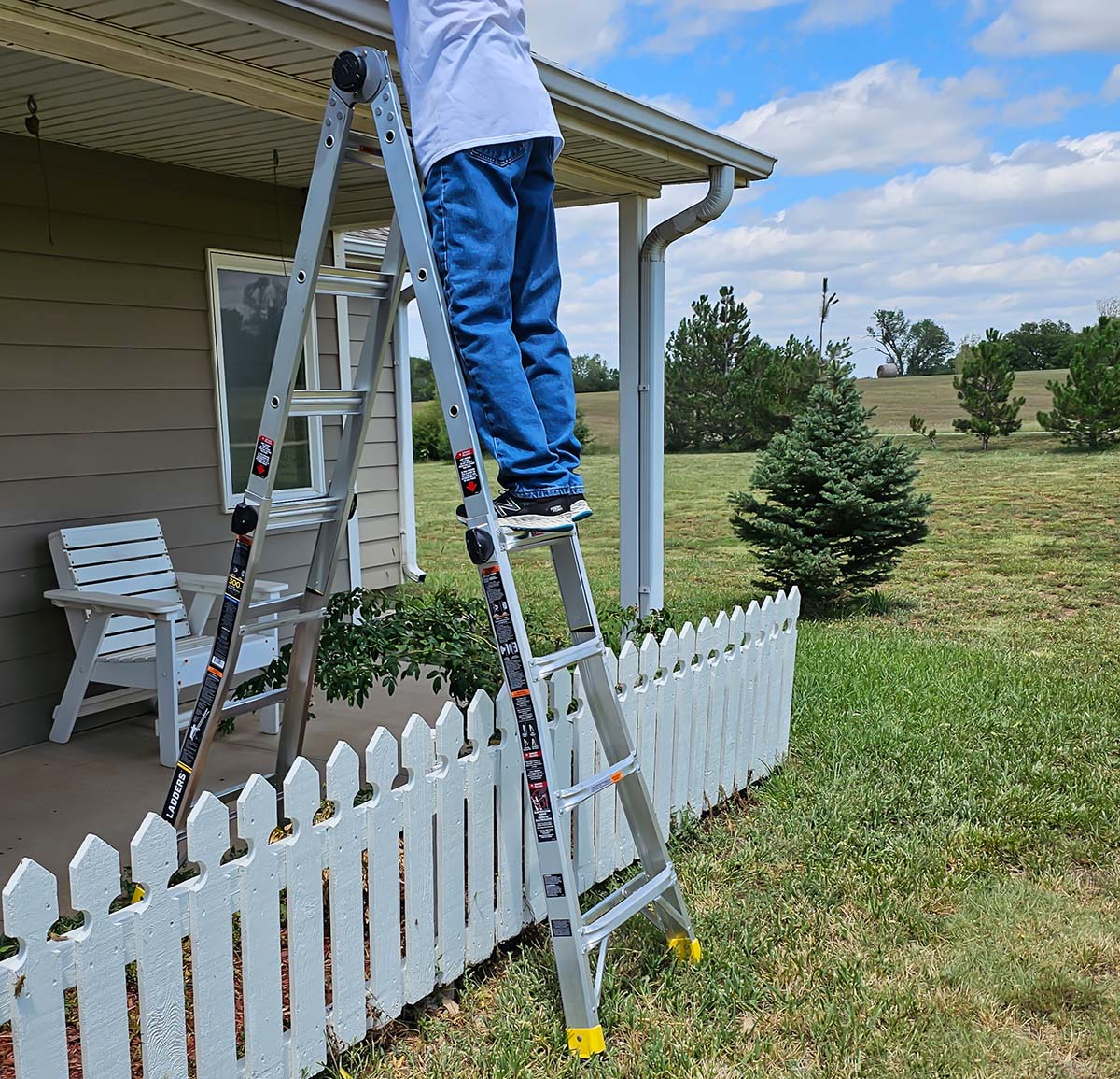 A person climbing the Gorilla ladder while it's set up over a fence in stairway position with one side on a porch