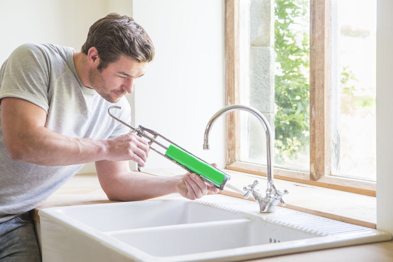 Man caulking around an enamel kitchen sink basin