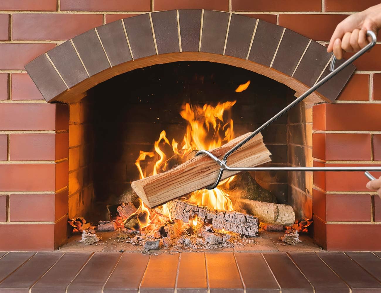 A person using the best fire pit tongs to add a log to a fire in a fireplace.