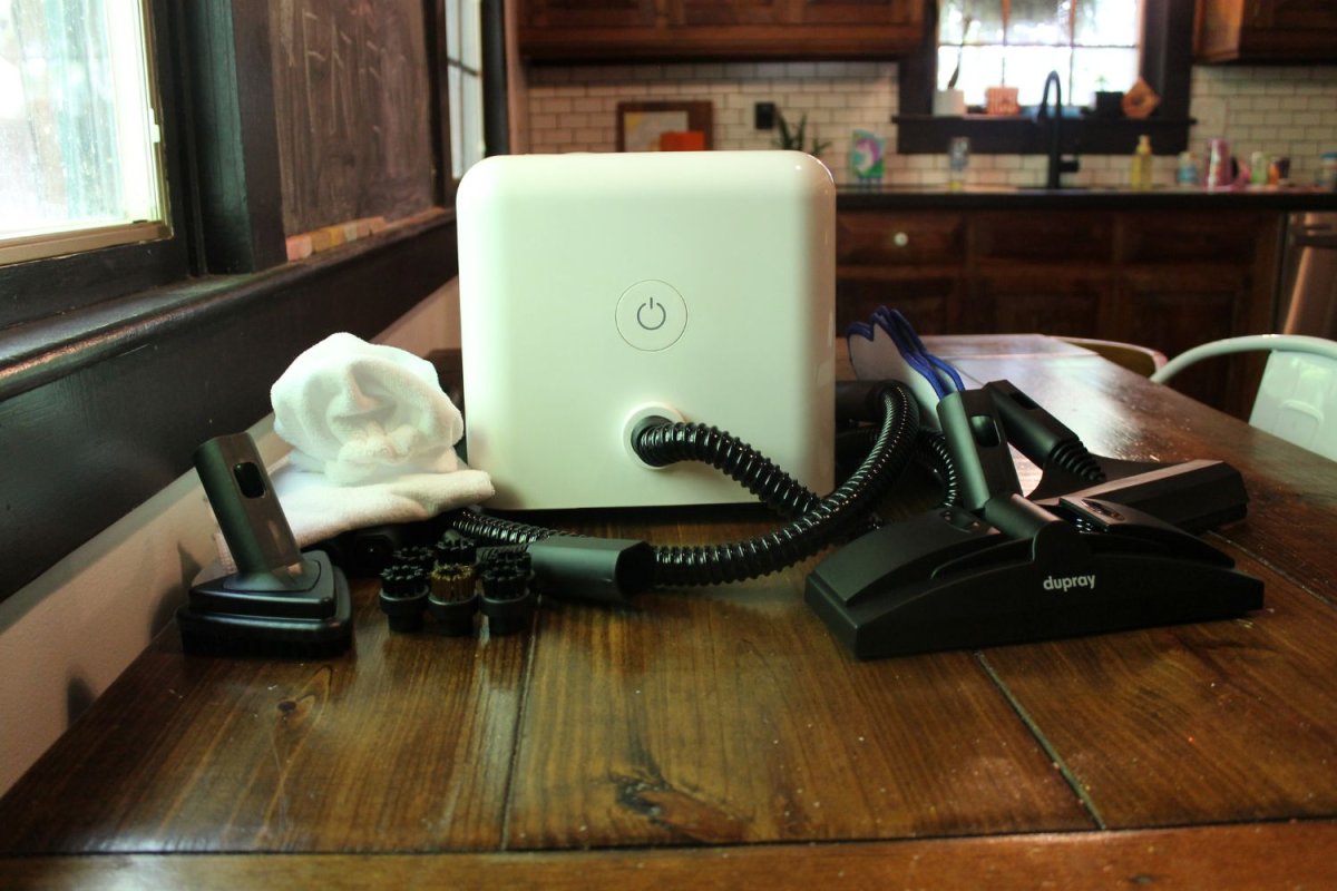 The Dupray Neat steam cleaner on a wood dining table with its included accessories