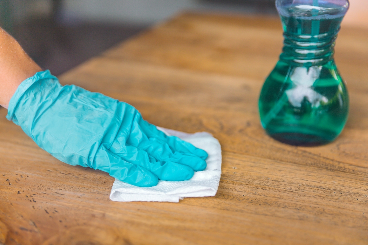 Gloved hand using towel to clean wood