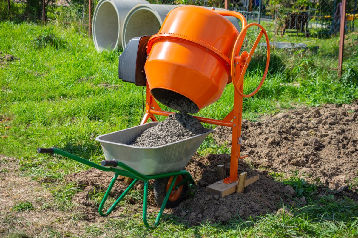 concrete is loaded into a cart from a 200 liter orange electric concrete mixer, photo taken on a sunny summer day outdoors