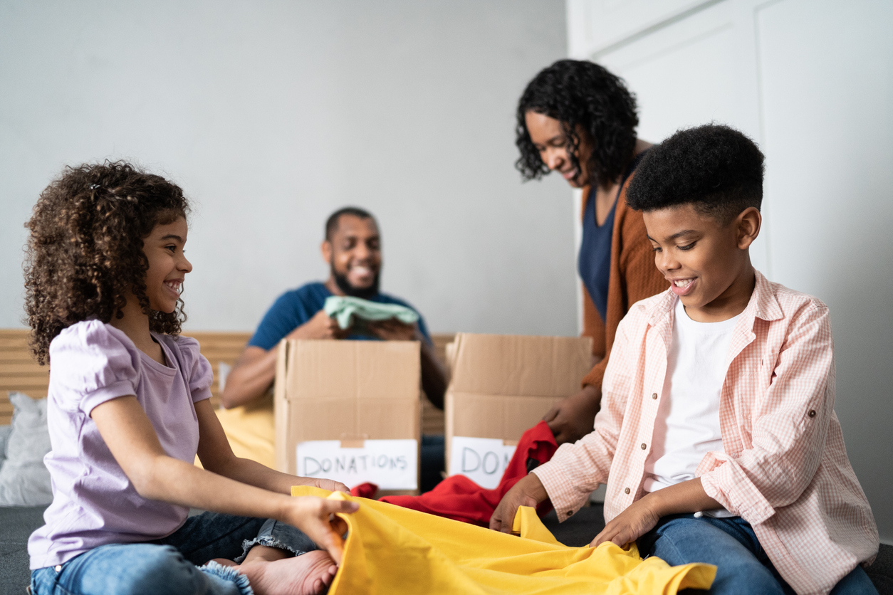 Parents with children sorting out clothes in boxes to donate at home