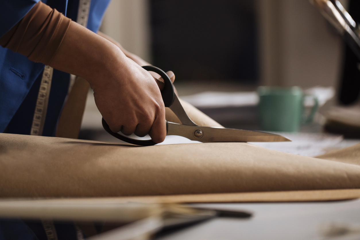 hands of woman cutting brown paper with scissors