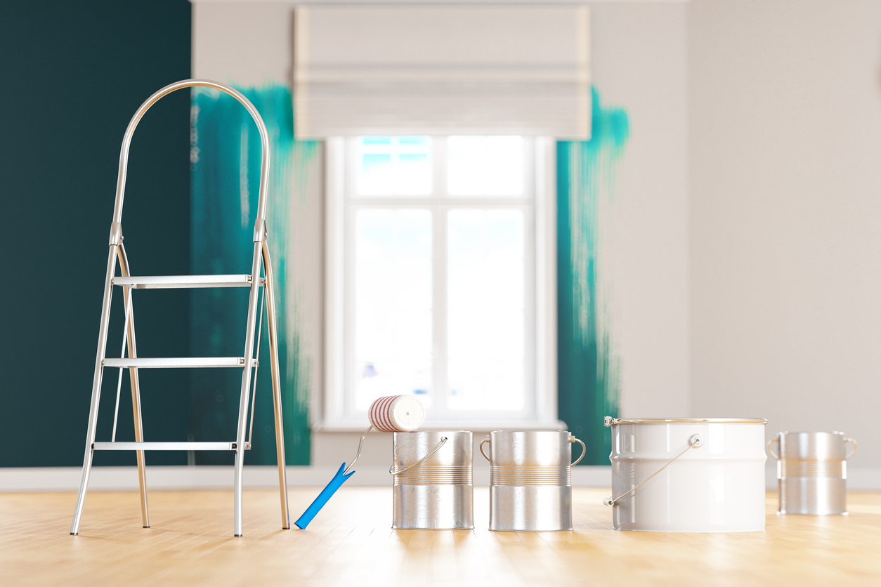 paint supplies in empty living room with wall in the background painted with half a second coat