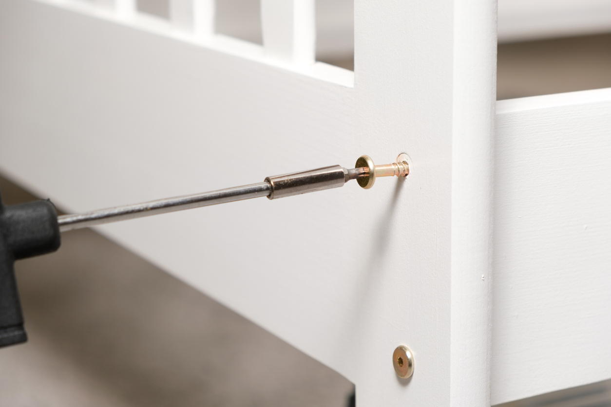 Close-up process of screwing a self-tapping screw into a white wooden bed with a screwdriver