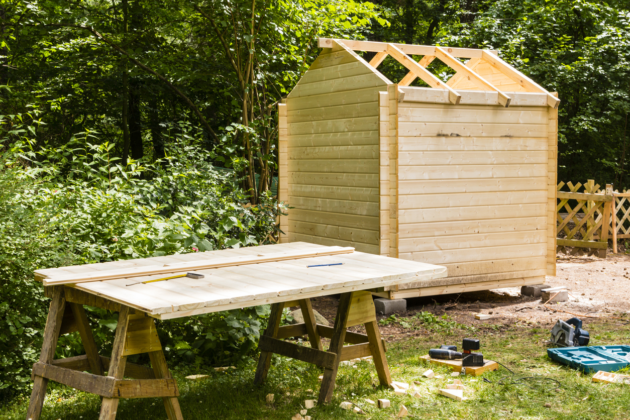 wooden-shed-in-progress-with-building-materials-around-it-and-bushes-behind-it