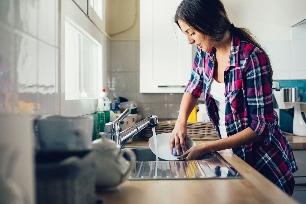 woman standing at kitchen sink rinsing a plate