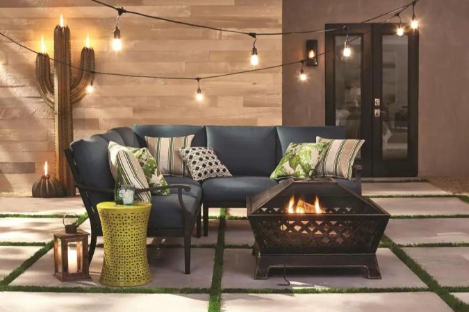 The best cheap fire pit housing a glowing fire next to an outdoor sectional on a cement patio.