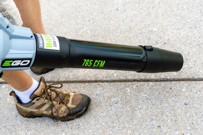 A person using the Ego Power+ 650 CFM 56V Leaf Blower to clean a crack in a sidewalk or driveway.