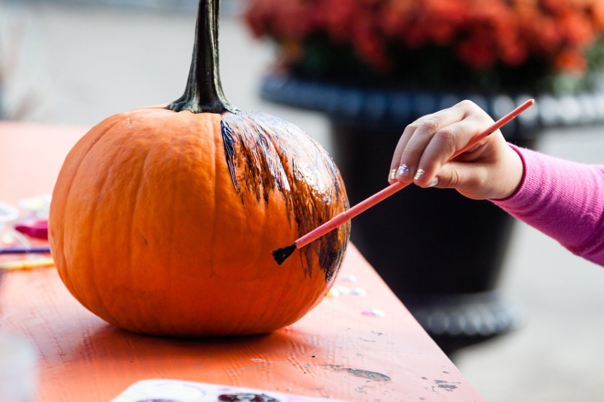 A young girl painting a medium-size pumpkin black with a watercolor brush.